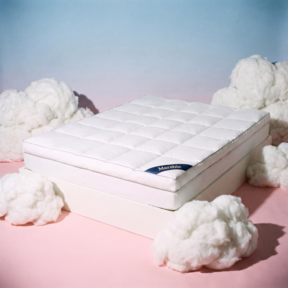 The Marshie Topper on a white bed base surrounded by soft white clouds on a pink and blue set