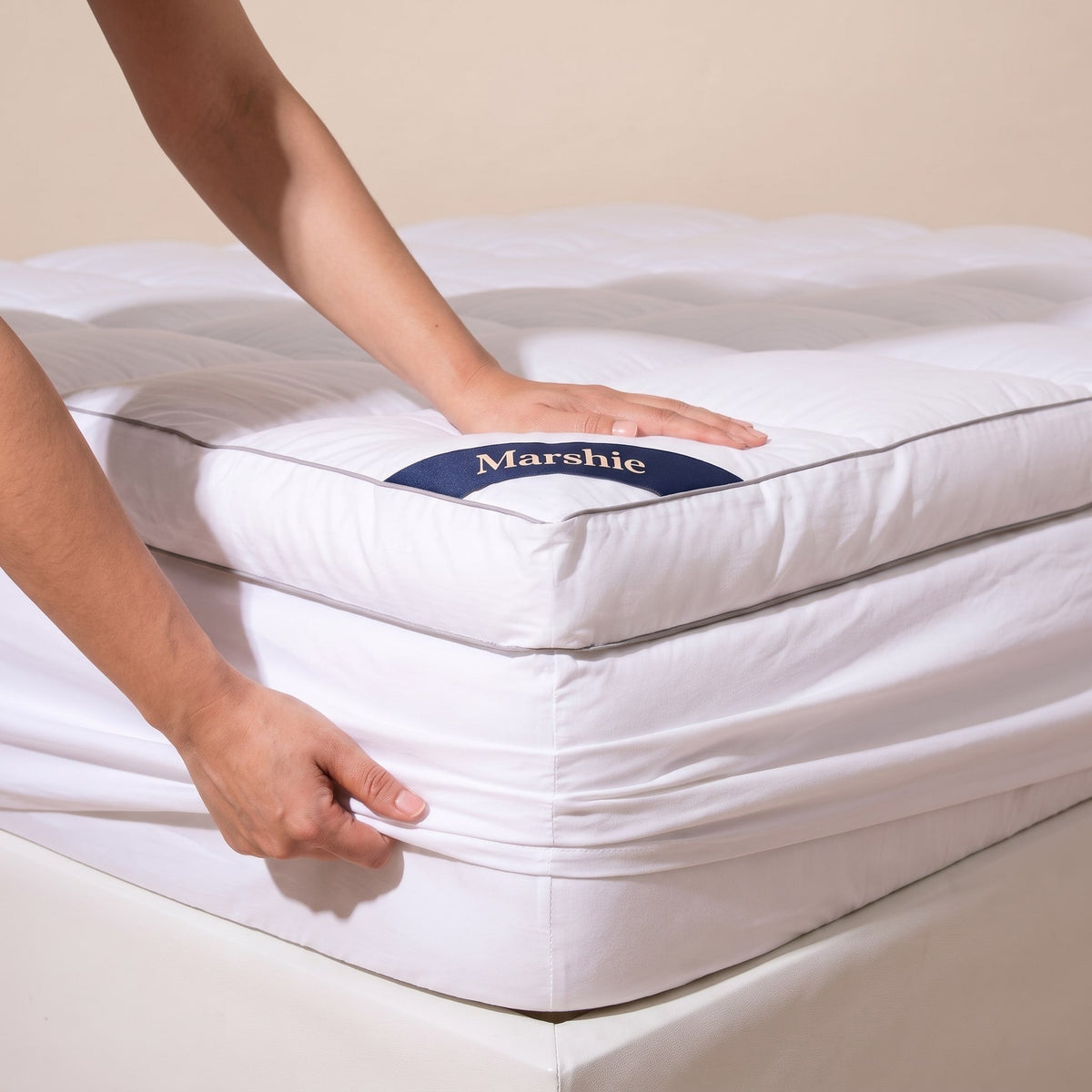 Hands pulling the deep elasticated skirt of the Marshie Topper over a mattress corner