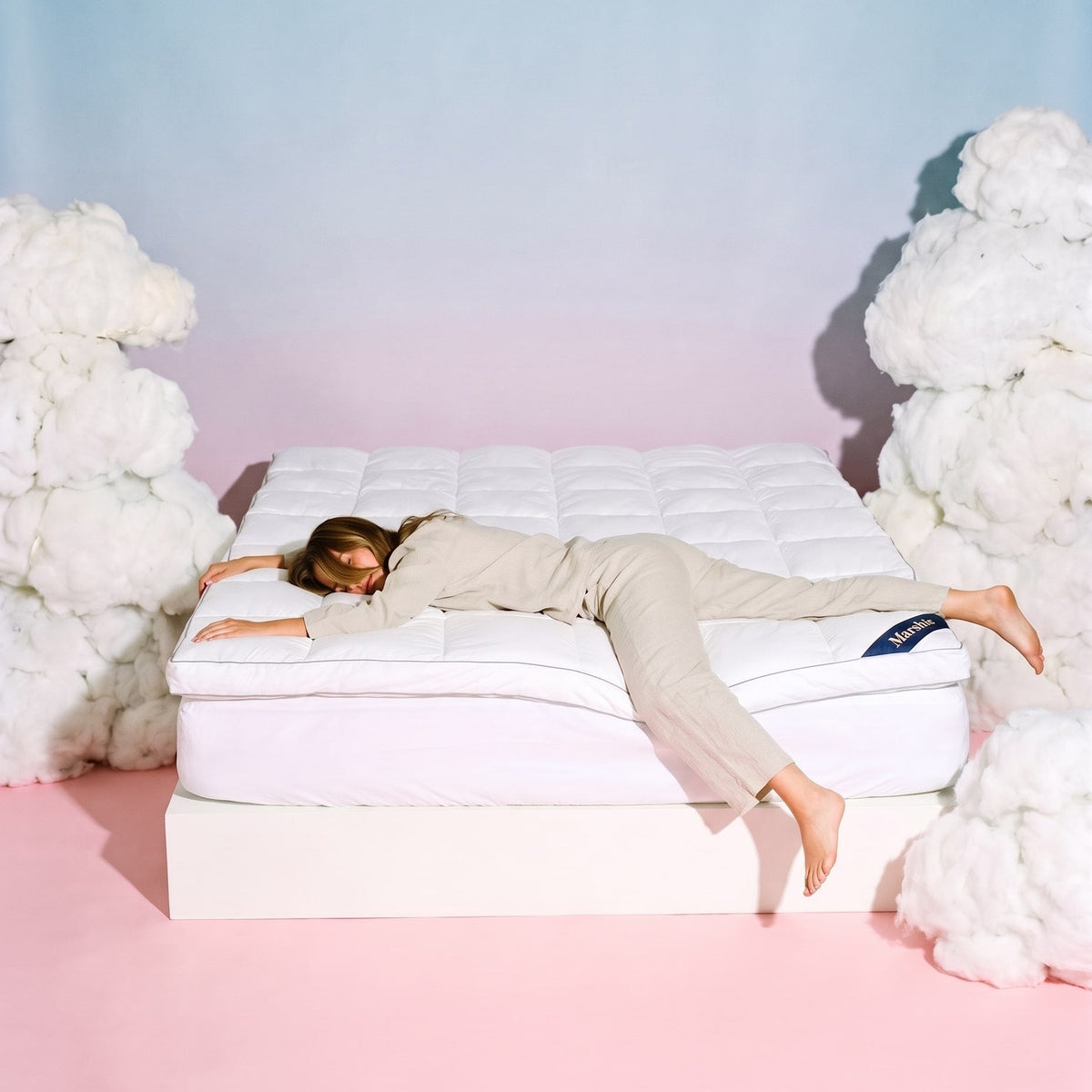 Woman lying face down across a bed with the Marshie Topper between white clouds