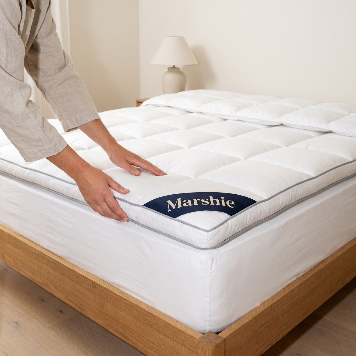 Hands smoothing the Marshie Topper over a mattress on an oak bed frame
